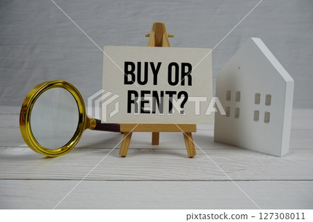 Buy or Rent? text on paper card with white house model and magnifying glass on wooden background Buy or Rent? text on paper card with white house model and magnifying glass on wooden background 127308011