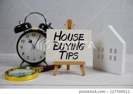House Buying Tips text on paper card with alarm clock, white house model and magnifying glass on wooden background House Buying Tips text on paper card with alarm clock, white house model and magnifying glass on wooden background 127308012
