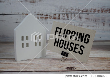 Flipping Houses on paper card with white house model on wooden background 127308029