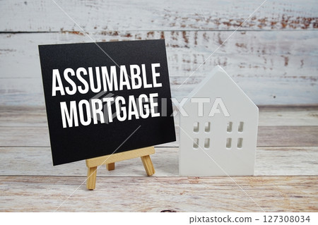 Assumable Mortgage on paper card with white house model on wooden background 127308034