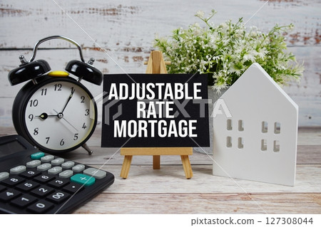 Adjustable Rate Mortgage on paper card with white house model, calculator and alarm clock on wooden background 127308044