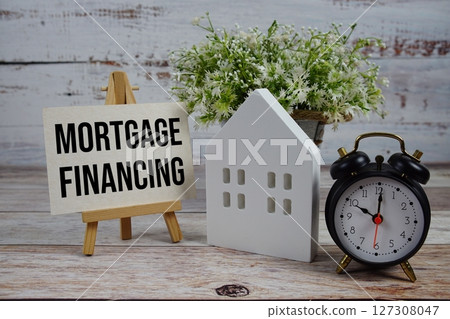 Mortgage Financing on paper card with alarm clock and white house model on wooden background 127308047