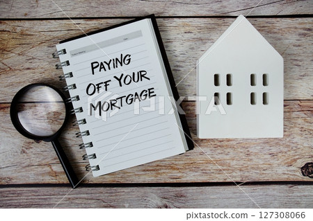 Paying Off Your Mortgage text on paper notebook with white house model and magnifying glass on wood background 127308066
