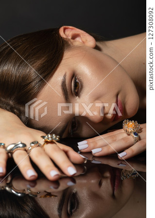 Studio portrait of beautiful and sexy brunette woman with fancy make-up and various rings on her fingers 127308092