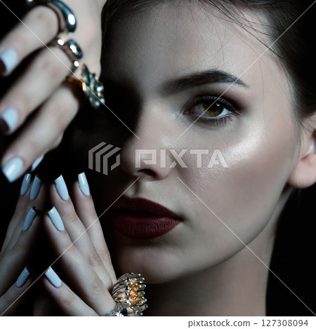 Studio portrait of beautiful and sexy brunette woman with fancy make-up and various rings on her fingers 127308094