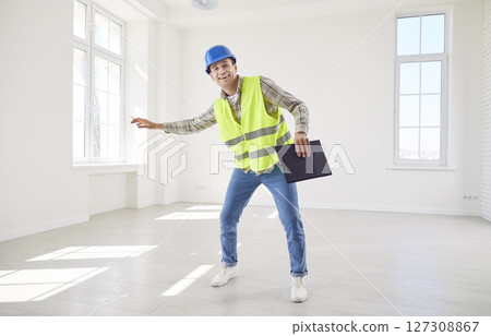 Young happy foreman working in empty new apartment wearing uniform and helmet. Young happy foreman working in empty new apartment wearing uniform and helmet. 127308867