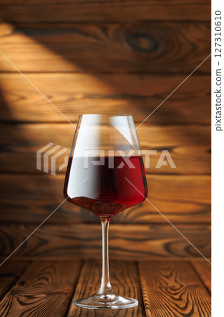 glass red wine basks in dramatic beam of light, sitting elegantly on rustic wooden table 127310610