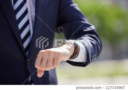 一位身著西裝的年輕商人在商業區看著手錶 127310967