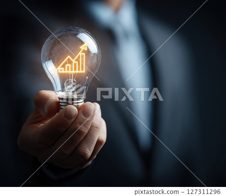 Businessman holding light bulb with growing graph inside symbolizing innovation and success 127311296