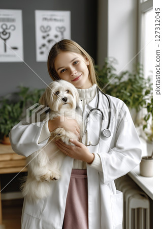Young veterinarian trainee holding a small dog in a bright clinic with plants and artwork Young veterinarian trainee holding a small dog in a bright clinic with plants and artwork 127312045