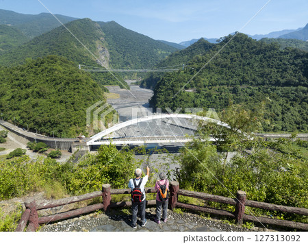 A couple of seniors with backpacks stand against a mountain landscape 127313092