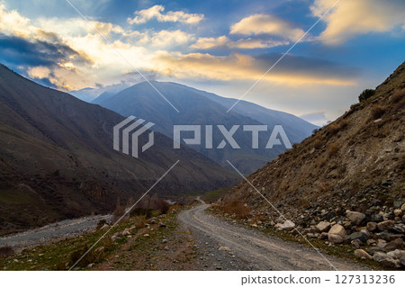 Serene mountain gravel road alongside a flowing river in nature at evening in Kyrgyzstan 127313236