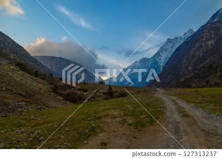 Majestic mountain range with dirt road in serene valley at springtime evening 127313237