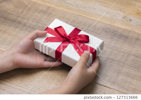 A gift box with a red ribbon being presented by both hands A gift box with a red ribbon being presented by both hands 127313666