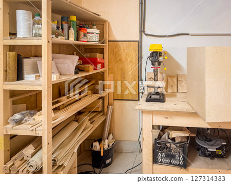 Organized woodworking shop featuring tools, drill press, materials, and shelving packed with supplies, set in a clean and functional creative workspace Organized woodworking shop featuring tools, drill press, materials, and shelving packed with supplies, set in a clean and functional creative workspace 127314383