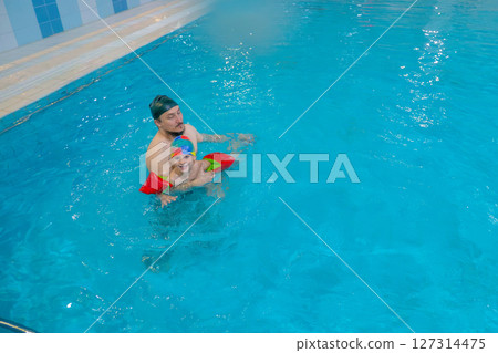 Dad and child are swimming indoor pool. Father teachs to swim. Dad and child are swimming indoor pool. Father teachs to swim. 127314475