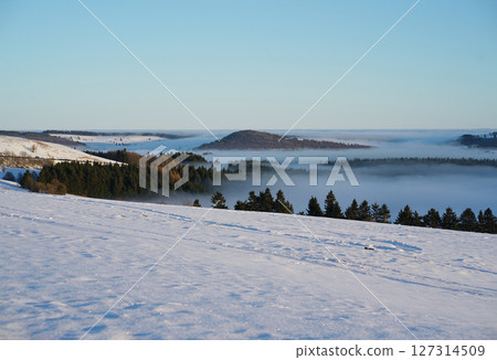 Winter landscape, a ski track in the snow, mountains of the Wasserkuppe. Wasserkuppe, in Hesse, Germany. Traveling to the mountains in the winter. Winter landscape, a ski track in the snow, mountains of the Wasserkuppe. Wasserkuppe, in Hesse, Germany. Traveling to the mountains in the winter. 127314509
