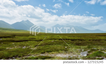 Rolling green hills meet dramatic, dark mountains under a brooding, cloudy sky. A peaceful, yet powerful landscape. Rolling green hills meet dramatic, dark mountains under a brooding, cloudy sky. A peaceful, yet powerful landscape. 127315245