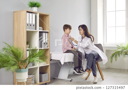 Woman doctor with stethoscope listening to breath or heartbeat of little boy patient Woman doctor with stethoscope listening to breath or heartbeat of little boy patient 127315497