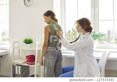 Pediatrician using stethoscope checks lungs and heartbeat of schoolgirl during medical examination. Pediatrician using stethoscope checks lungs and heartbeat of schoolgirl during medical examination. 127315501