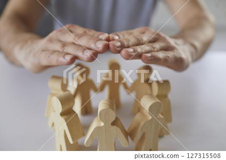 Male hands covering and protecting team of people made of wood Male hands covering and protecting team of people made of wood 127315508