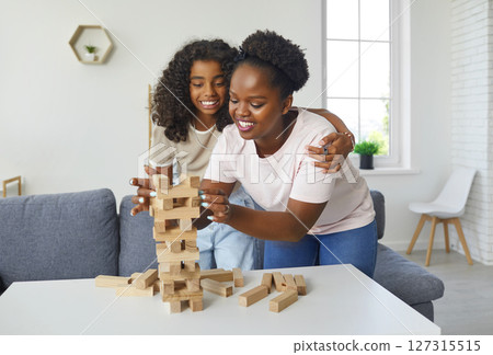 Happy African American mother and daughter playing board game and having fun at home 127315515