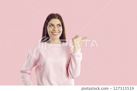 Young woman smiling and pointing thumb at copy space for your great offer or promotional banner Young woman smiling and pointing thumb at copy space for your great offer or promotional banner 127315519