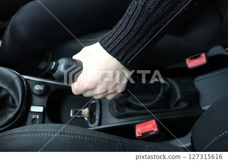 A hand positioned on the gear shift within the stylish and modern interior of a car 127315616