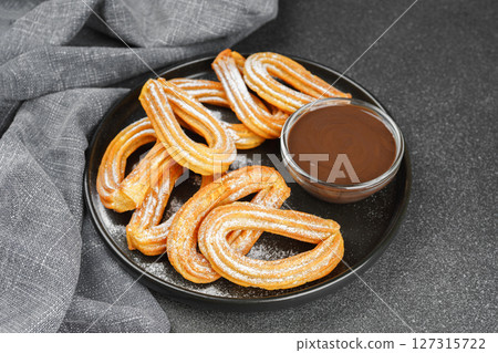 Traditional spanish dessert churros, fried dough pastry and chocolate sause on black background Traditional spanish dessert churros, fried dough pastry and chocolate sause on black background 127315722