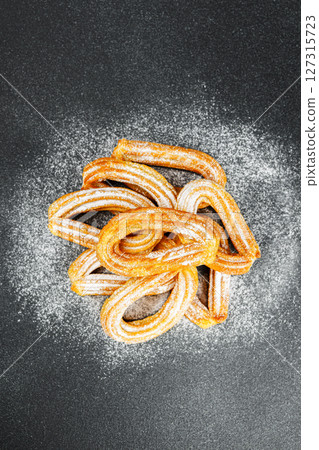 Traditional spanish dessert churros, fried dough pastry dusted with powdered sugar, black background Traditional spanish dessert churros, fried dough pastry dusted with powdered sugar, black background 127315723