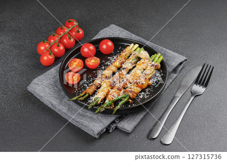 Grilled asparagus wrapped with bacon on black plate with cherry tomatoes on black background Grilled asparagus wrapped with bacon on black plate with cherry tomatoes on black background 127315736