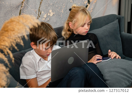 Children Laptop Couch - Two children sit on a couch, both using laptops, likely for schoolwork or entertainment. 127317012