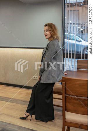 Woman Blazer Office: Woman rests on table in office, looking back during break/meeting, wearing blazer. Woman Blazer Office: Woman rests on table in office, looking back during break/meeting, wearing blazer. 127317094