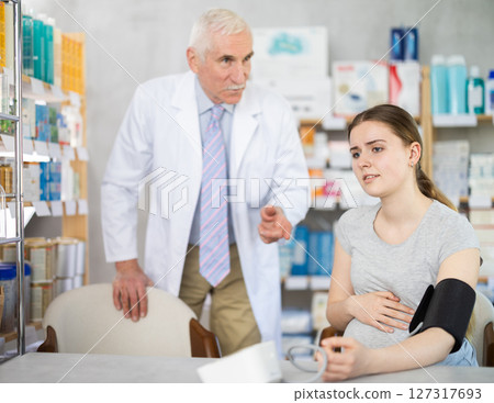 Sad pregnant woman having blood pressure measured and male pharmacist talking 127317693