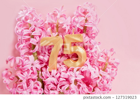 Number 75 seventy five golden celebration birthday candle on Pink flowers Background. 75 years birthday. concept of celebrating birthday, anniversary, important date, holiday milestone 127319023