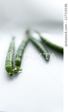 Close-up of fresh green pea pods on a white background with shallow depth of field, ideal for healthy eating concepts. Close-up of fresh green pea pods on a white background with shallow depth of field, ideal for healthy eating concepts. 127319186
