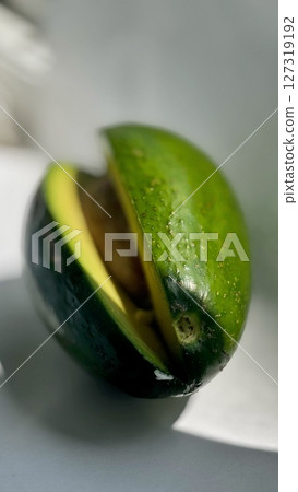 Close-up of a sliced ripe avocado exposing the seed, displayed on a clean white surface with natural lighting and shadows. Close-up of a sliced ripe avocado exposing the seed, displayed on a clean white surface with natural lighting and shadows. 127319192