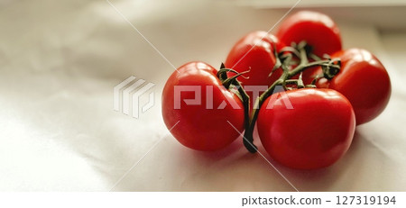 A diagonal group of vine tomatoes rests on a clean background, with ripe red skin and green stems arranged naturally. 127319194