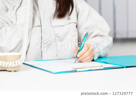 A woman in work clothes taking a phone call and taking notes 01 A woman in work clothes taking a phone call and taking notes 01 127320777
