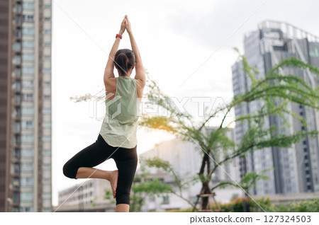 Asian woman in 30s fitness yoga workout. Stretching exercise reduces medical injury risk shoulder pain muscle strain inflammation. Healthy lifestyle wellness healthcare in urban city at sunset 127324503