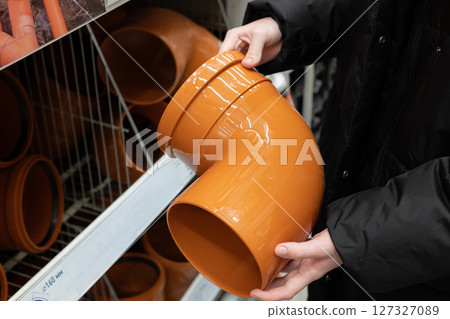 Person holding yellow PVC pipe fitting while shopping in home improvement store aisle during daytime Person holding yellow PVC pipe fitting while shopping in home improvement store aisle during daytime 127327089