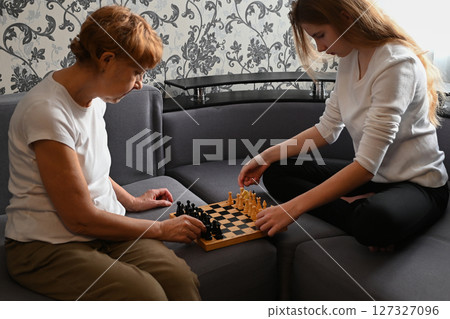 Engaging chess match between two players on a cozy couch in a living room during the afternoon Engaging chess match between two players on a cozy couch in a living room during the afternoon 127327096