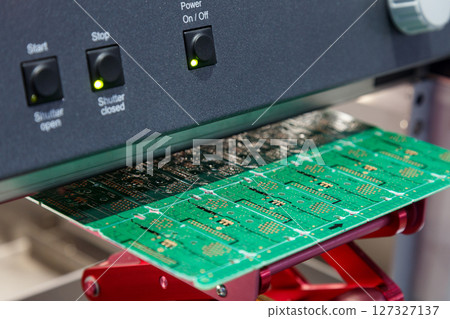 electronic circuit board under processing machine. Close-up of green PCB manufacturing stage with illuminated control panel. Electronic components production and assembly line. 127327137