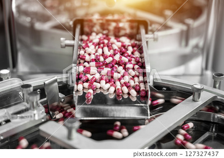 Close up of pink and white capsules pills in the pills packaging machine, pharmacy medicine capsule pill in production line at medical factory. 127327437