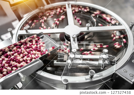 Pink and white capsules pills in the pills packaging machine, pharmacy medicine capsule pill in production line at medical factory. Pink and white capsules pills in the pills packaging machine, pharmacy medicine capsule pill in production line at medical factory. 127327438