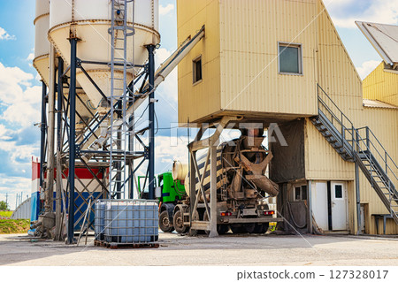 Concrete mixer truck in front of a concrete batching plant, cement factory. Loading concrete mixer truck. Close-up. Delivery of concrete to the construction site. Monolithic concrete works. 127328017