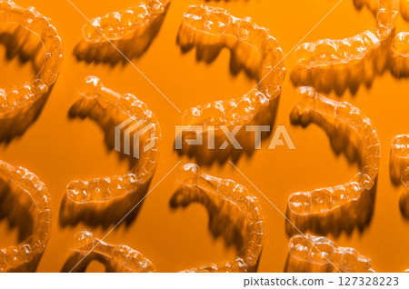 Invisible transparent aligners for teeth alignment of the lower and upper jaw. Wax models of teeth, top view, on orange background 127328223