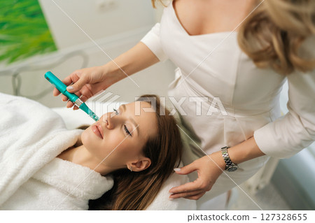 Top view of female patient receiving rejuvenation treatment in cosmetology clinic. Professional beautician performing mesotherapy treatment to young woman focusing on skin rejuvenation, hydration. Top view of female patient receiving rejuvenation treatment in cosmetology clinic. Professional beautician performing mesotherapy treatment to young woman focusing on skin rejuvenation, hydration. 127328655