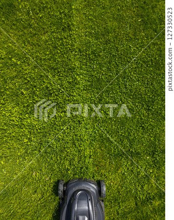 Lawn mower cutting grass on a sunny day in peaceful garden, high angle view Lawn mower cutting grass on a sunny day in peaceful garden, high angle view 127330523