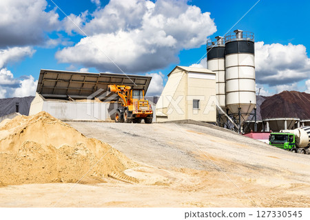 A large front loader transports materials in a concrete production plant. Production of concrete. Transportation of bulk materials. Construction equipment. Bulk cargo transportation. 127330545